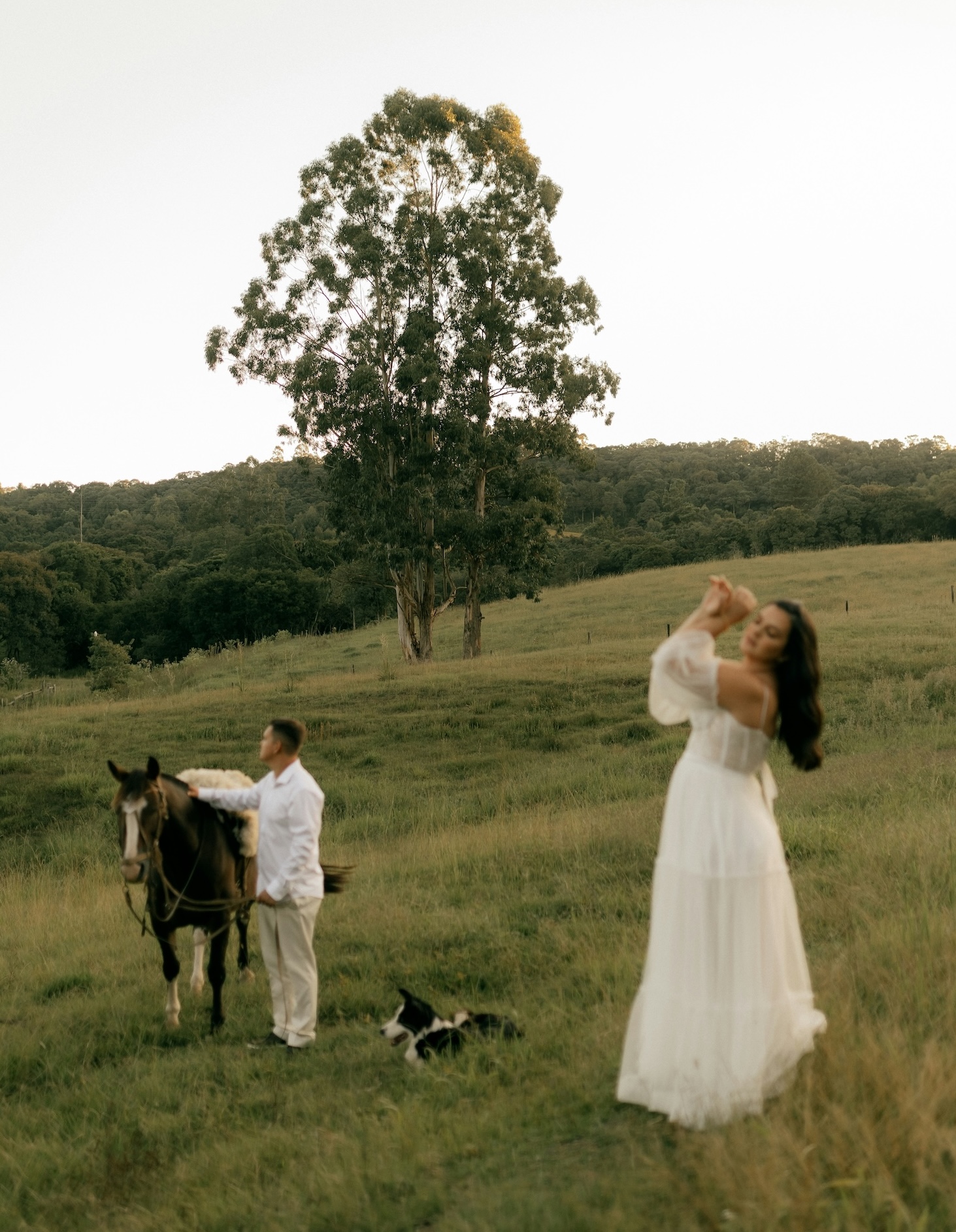 Wedding photographer's blog image of a bride dancing in a countryside field at golden hour while the groom stands with a horse, an example of a wedding worth blogging.