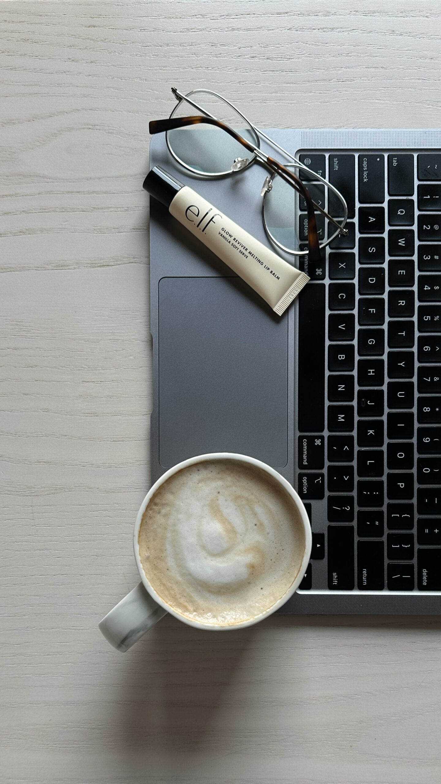 Laptop keyboard with a latte, glasses, and lip balm nearby during a Pinterest strategy session
