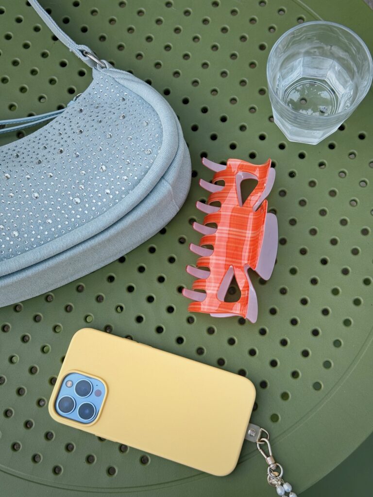 Aesthetic photo for social media featuring a yellow phone, orange hair clip, and blue handbag on a green table, representing lifestyle visuals business owners can use to make social media more engaging.