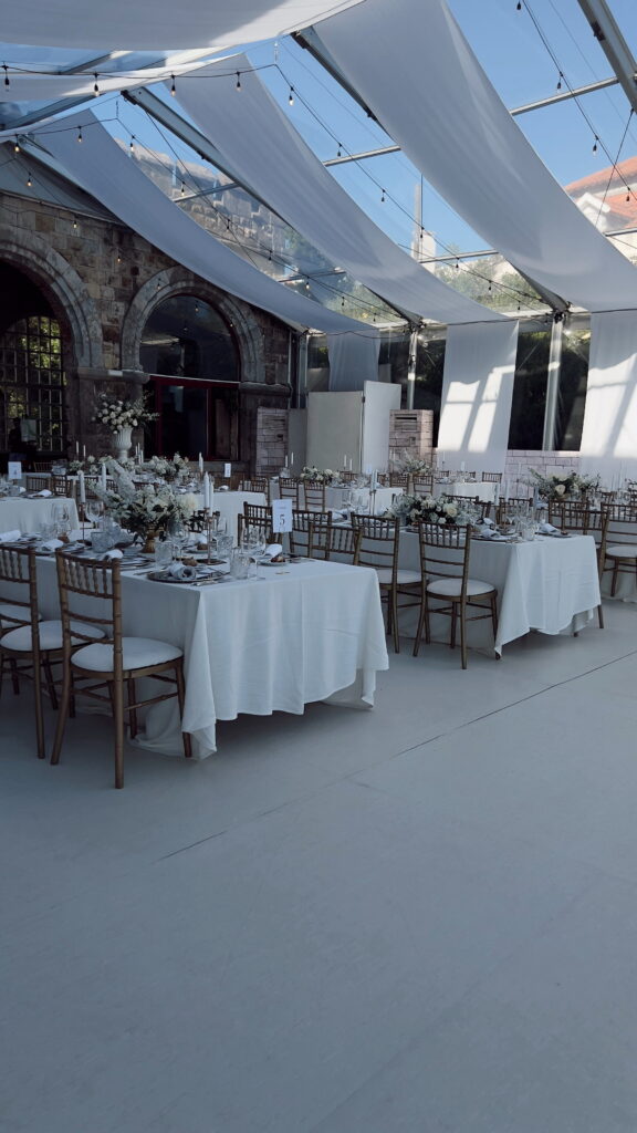 Elegant wedding reception setup under a clear tent with chiavari chairs and white florals — ideal for luxury wedding photographer blog posts about venue selection and getting-ready spaces