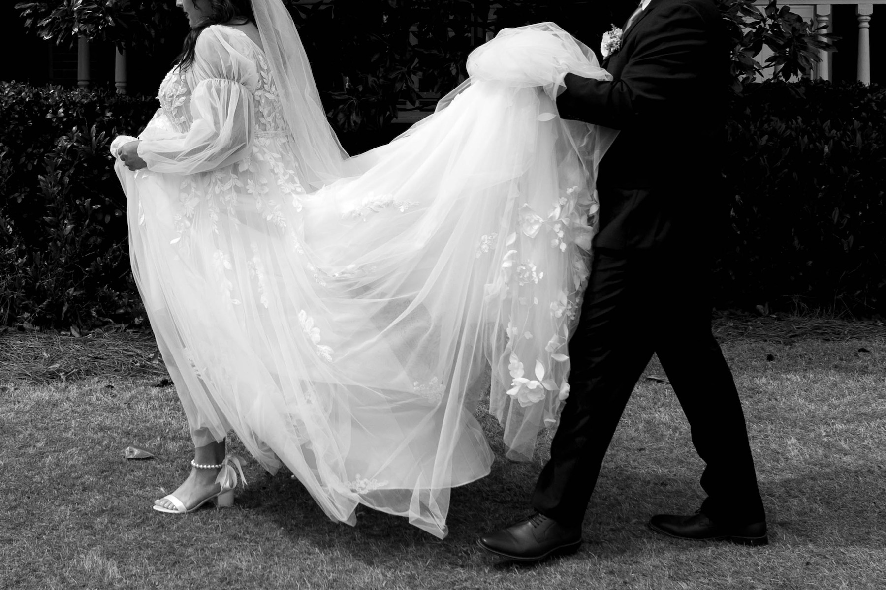 Black and white photo of a bride and groom walking as he lifts her floral tulle gown — wedding photography blog content for photographers looking to attract editorial and luxury wedding bookings